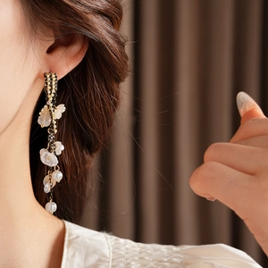 Detail of floral pearl tassel earrings featuring elegant long metallic fringe on a model