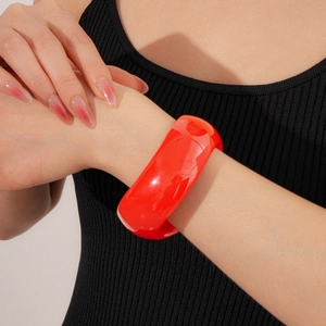 Detail view of bold red acrylic wave bangle on model wrist with minimalist grey background