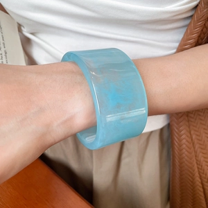 Close-up of a wide light blue resin bangle with marble texture worn on wrist