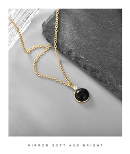 Detail of a round black gemstone pendant necklace with gold chain and white zircon inlay