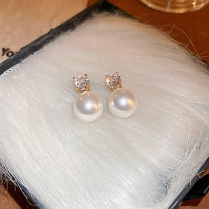 Close-up of elegant pearl stud earrings with sparkling zircon on a soft white plush background