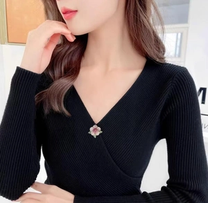 Pink camellia brooch with green leaves pinned on a black V-neck sweater detail
