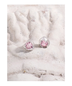 Macro shot of pink heart-shaped zircon earrings on white textured stone surface