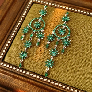 Close-up of silver floral tassel earrings with green crystals on a vintage velvet display