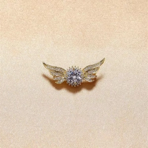 Elegant gold angel wing brooch with sparkling rhinestones on beige fabric background