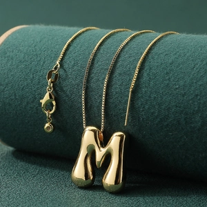 Polished gold 3D letter M pendant necklace with fine chain on green velvet display