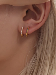 Dettaglio di orecchini a cerchio placcati oro con zirconi colorati e bianchi su modella
