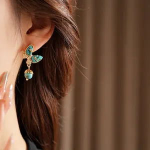 Boucles d'oreilles papillon dorées avec turquoise et zircon sur modèle pour look élégant