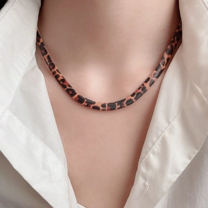 Detail einer flachen Schlangenkette mit Leopardenmuster an einem weißen Hemdkragen