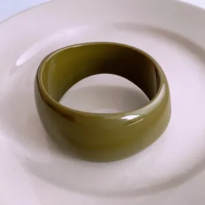Bracelet jonc épais vert olive en acrylique poli sur un plateau en céramique blanche
