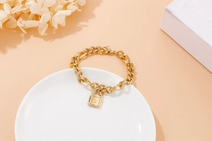 Makroaufnahme von goldener Gliederkette mit Schloss-Anhänger auf minimalistischem Tablett