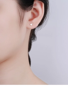 Close-up of minimalist tiny silver butterfly stud earrings on a female model's ear
