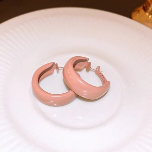 Macro detail of Morandi pink C-shaped earrings on textured white ceramic tray