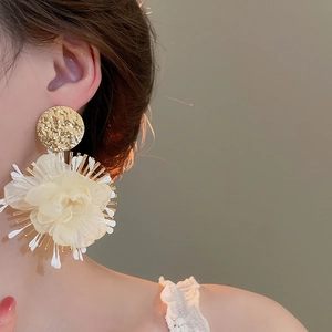 Close-up of large chiffon flower earrings with gold textured metal on model