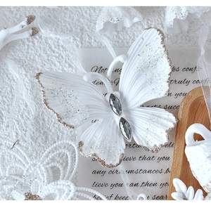Detailed view of a white butterfly ornament with gold glitter edges and silver rhinestones
