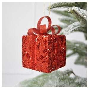 Close-up of red sequined gift box ornament hanging on a frosted Christmas tree branch