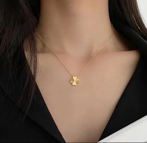 Close-up of a gold 18k four-leaf clover necklace worn on neck with textured clover pendant