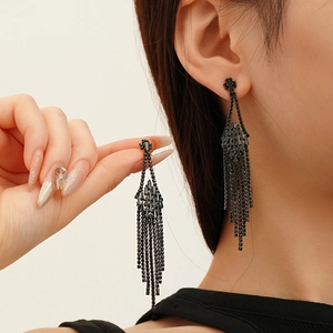 Détail de longues boucles d'oreilles noires à glands avec zircons et strass géométriques