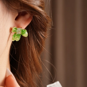 Close-up of gold-plated flower earrings with green stones worn by a model