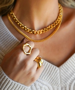 Détail de chaînes gourmettes dorées et bagues géométriques sur un pull en maille