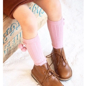 Detail of pink ribbed baby knee-high socks with cute pom-pom accents and soft texture