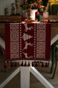 Close-up of red Christmas table runner featuring white reindeer motifs and festive tassels