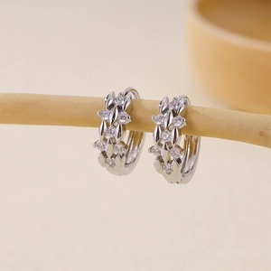 Pendientes de aro plateados con diseño cruzado y circonitas sobre una rama de madera