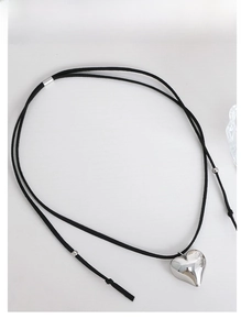 Detailed view of large silver heart pendant on black faux suede cord necklace on white background