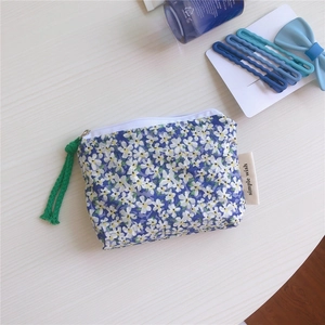 Close-up of blue floral cotton mini pouch with white zipper and green woven strap detail