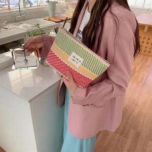 Detail of colorful striped woven toiletry bag with zipper and logo held by model