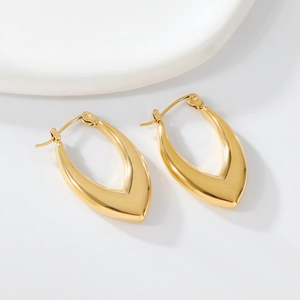 Macro detail of polished gold V-shaped irregular earrings on a minimalist white tray