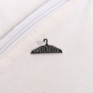 Macro shot of Pro-Choice enamel pin in clothes hanger shape on white canvas