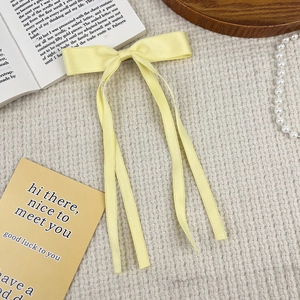 Detailed close-up of a pale yellow satin bow hair clip with long elegant ribbons