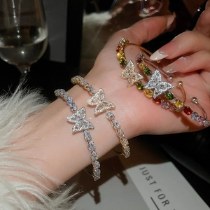 Dettaglio di tre bracciali a farfalla in zirconia con finiture oro e argento al polso