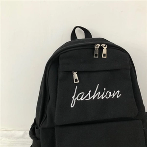 Close-up of black canvas backpack featuring white fashion embroidery and zipper detail