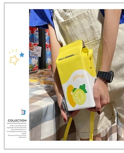 Detail view of lemonade milk carton crossbody bag with yellow strap in lifestyle setting