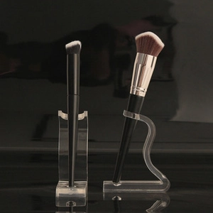 Acrylic makeup brush display stand with black and gold brushes on a dark surface