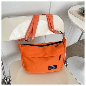 Detail of vibrant orange canvas crossbody bag with black zipper hanging on a white chair