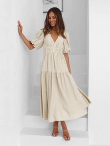 Detail of elegant beige V-neck dress with puff sleeves and layered skirt on a staircase
