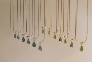Detail of drop-shaped green and blue pendants on gold and silver snake bone chains