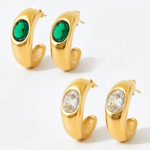 Detailed view of C-shaped gold earrings with emerald green and white oval gemstones