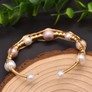 Handmade woven gold wire bracelet with natural white and pink pearls on wood background