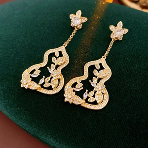 Gros plan de boucles d'oreilles gourde en or avec détails floraux sur velours vert