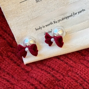 Detail of pearl earrings featuring red velvet bows on a cozy knit background texture