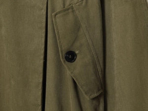 Gros plan d'un trench-coat vert militaire avec texture en toile épaisse et bouton noir précis