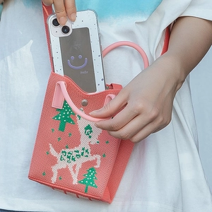 Detail showing a pink knitted mini tote bag with deer pattern and a phone being placed inside