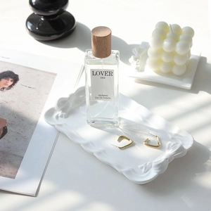 Detail view of a white plaster bow tray displaying perfume and jewelry on a desk