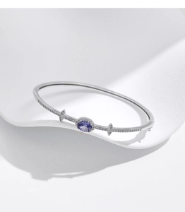 Macro detail of silver bangle featuring an oval purple gemstone and pavé-set crystals