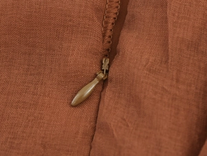 Close-up of concealed zipper and textured brown fabric on a pleated V-neck dress