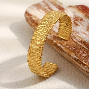 Détail de la texture ondulée verticale irrégulière sur le bracelet jonc en acier plaqué or
